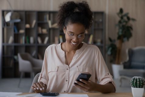 Uma Mulher fazendo cálculos enquanto olha para o smartphone.