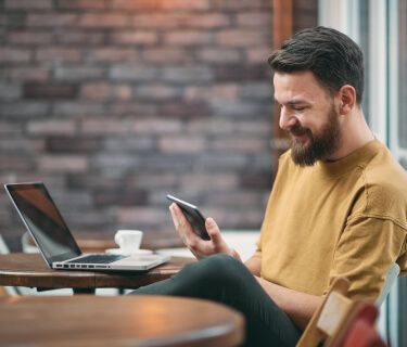 Homem com uma xícara de café, sorrindo enquanto olha para o smartphone.