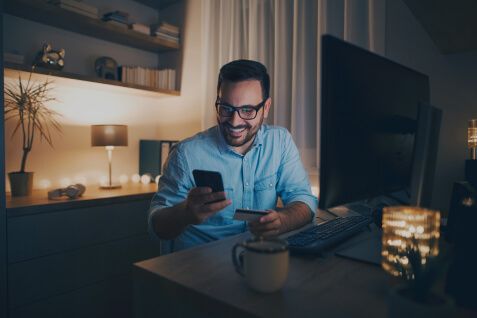 Homem sorrindo ao olhar para o smartphone.