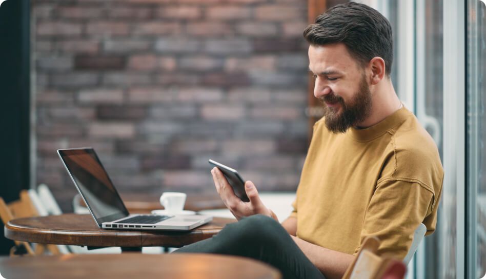 Homem com uma xícara de café, sorrindo enquanto olha para o smartphone.