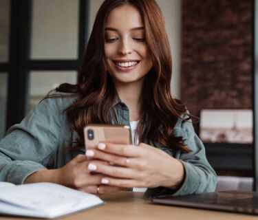 Mulher sorrindo enquanto olha para o smartphone.